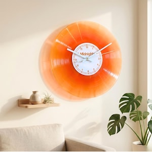 Könnte beinhalten: Eine runde Wanduhr aus einer durchscheinenden orangefarbenen Schallplatte. In der Mitte befindet sich ein weißes Zifferblatt mit schwarzen Zahlen von 1 bis 12, dem Wort Midnight in orangefarbenem Text und drei dünnen weißen Zeigern.