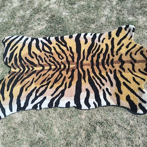 May include: A tiger-striped rug with a tan, brown, and black pattern. The rug is shaped like a tiger skin, with a head and paws. The rug is made of a soft material and is suitable for a living room or bedroom.