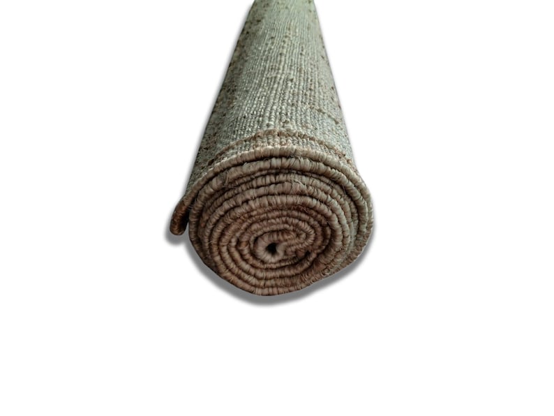 Peut inclure: Tapis de sol enroul&eacute; avec un aspect textur&eacute; et tiss&eacute;. Le tapis est principalement de couleur beige clair avec des bords marron plus fonc&eacute;s et une extr&eacute;mit&eacute; enroul&eacute;e, r&eacute;v&eacute;lant le dessous. Le tapis est sur fond blanc.