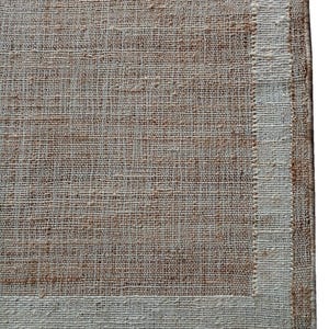 Peut inclure: Gros plan sur un tapis tiss&eacute; d'aspect naturel et textur&eacute;. Le tapis pr&eacute;sente un champ central brun clair avec une bordure cr&egrave;me. Le tissage est visible, cr&eacute;ant une esth&eacute;tique rustique et organique. Le design du tapis est simple et &eacute;l&eacute;gant.