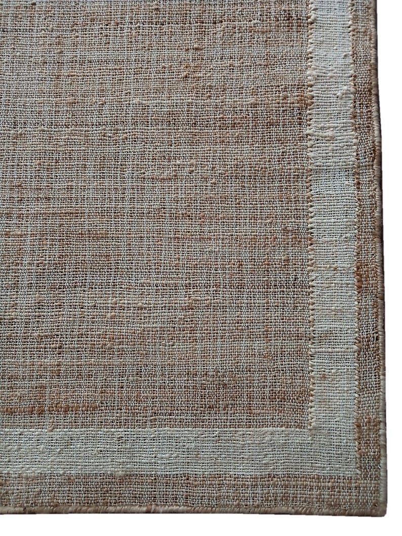Peut inclure: Gros plan sur un tapis tiss&eacute; d'aspect naturel et textur&eacute;. Le tapis pr&eacute;sente un champ central brun clair avec une bordure cr&egrave;me. Le tissage est visible, cr&eacute;ant une esth&eacute;tique rustique et organique. Le design du tapis est simple et &eacute;l&eacute;gant.