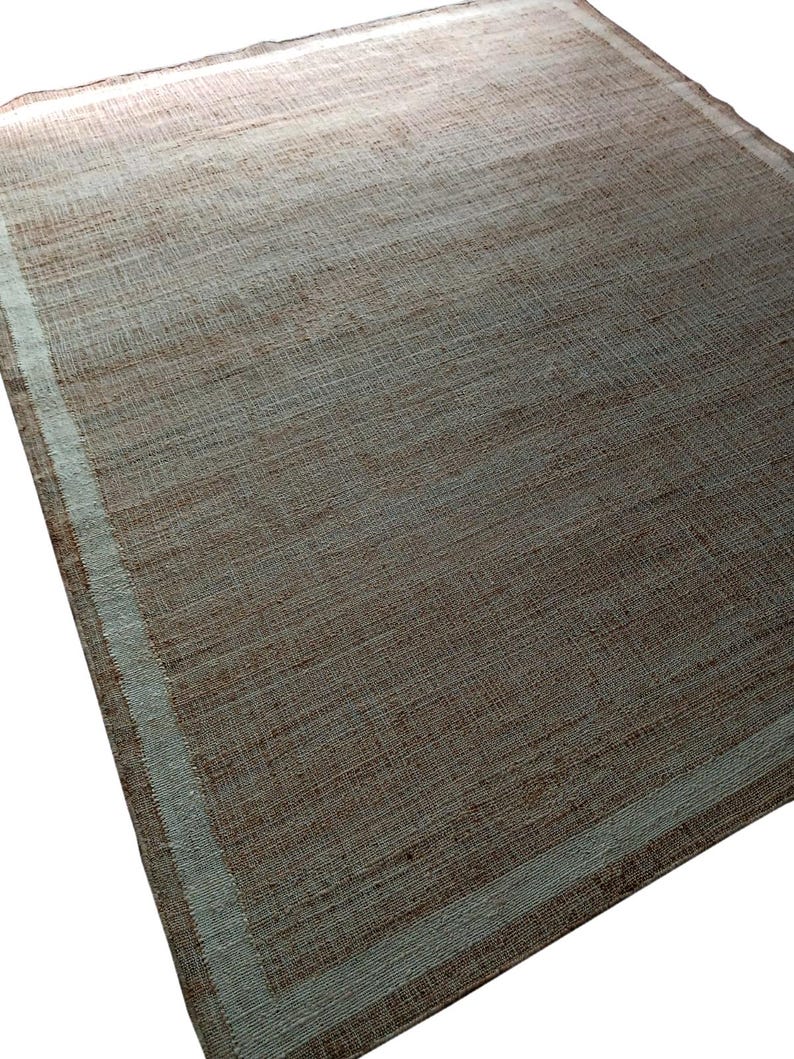 Peut inclure: Tapis rectangulaire tiss&eacute;, aux tons bruns et beiges. Il pr&eacute;sente une bordure beige clair qui encadre le corps principal. La texture semble rugueuse, avec des fils tiss&eacute;s visibles. Id&eacute;al pour un salon.