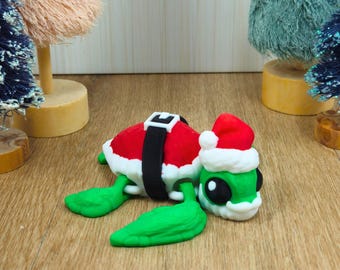 May include: A whimsical Christmas turtle figurine. The turtle is green with a Santa Claus hat and suit. The red suit has a white trim and a black belt. The turtle's head is also wearing a Santa hat.