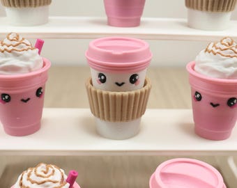 May include: A collection of pink toy coffee cups with kawaii faces. Some cups have whipped cream and a pink straw. One cup has a brown paper sleeve. The cups are arranged on white shelves.