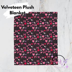 May include: A black blanket with a pattern of pink and red hearts and bows. The blanket is labeled "Velveteen Plush Blanket" in white text. The design is repeated across the entire surface of the blanket.