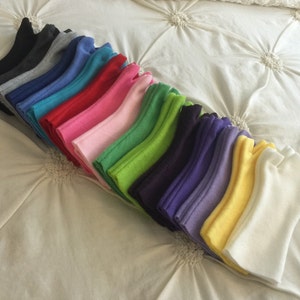 May include: A collection of colorful fleece gloves arranged in a diagonal row. The gloves are in various colors, including black, gray, blue, red, pink, green, purple, yellow, and white. The gloves are neatly folded and displayed on a white surface.
