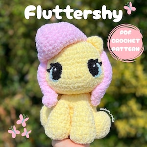 Peut inclure: Une peluche au crochet représentant un poney au corps jaune pâle et à la crinière rose clair. Le jouet présente de grands yeux noirs avec des reflets blancs et une finition en fil texturé. Le texte indique Fluttershy et PDF CROCHET PATTERN.