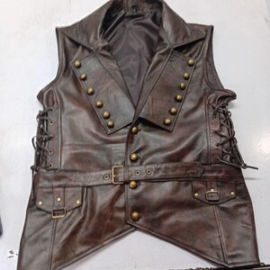 May include: A brown leather vest with a notched collar and brass-colored buttons. The vest has a belt with a buckle and two pockets. The sides of the vest have a lace-up design. This vest is a steampunk-inspired garment.