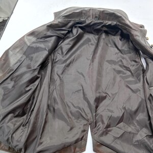 May include: A brown leather jacket with a dark brown satin lining. The jacket is open, revealing the interior lining and the button details along the front. The jacket appears to be vintage or pre-owned.