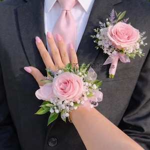 May include: A dark gray suit with a light pink tie and a matching rose boutonniere. A wrist corsage with a pink rose and greenery is also visible. The image suggests a formal event or celebration.