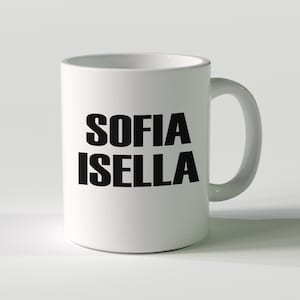 May include: White ceramic mug featuring the name "SOFIA ISELLA" in bold black lettering. The mug has a curved handle and a cylindrical design, ideal for tea, coffee, or other drinks.