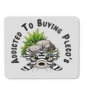 May include: A light grey square coaster featuring a cartoon zebra pleco fish. The fish is black and white with yellow eyes and whiskers. The text "ADDICTED TO BUYING PLECO'S" arches above the fish.