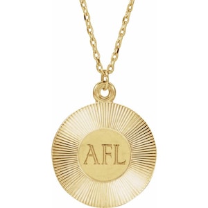 May include: A gold-colored necklace with a circular pendant. The pendant has a sunburst design with the letters "AFL" in the center. The chain is delicate and also gold-colored. The necklace is likely made of metal and is a piece of jewelry.