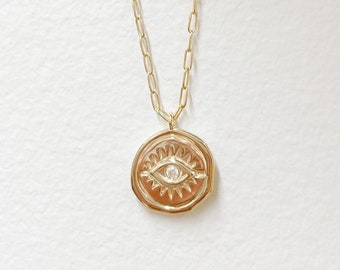 May include: A gold chain necklace with a gold pendant featuring a detailed eye design with a small diamond in the centre.