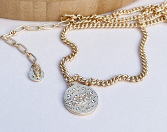 May include: Gold chain necklace with a round pendant featuring a crystal-encrusted evil eye design.