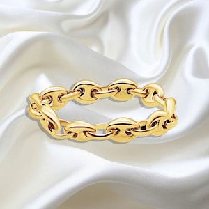 Könnte beinhalten: Ein goldenes Kettenarmband mit einem Ankerketten-Design. Das Armband ist aus poliertem Gold gefertigt und hat einen klassischen Look.