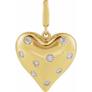 Può includere: Un ciondolo a forma di cuore dorato con diverse pietre preziose rotonde e trasparenti. Il ciondolo ha una superficie liscia e lucida e un anello nella parte superiore per attaccarlo a una catena o un braccialetto. Le pietre sono distribuite uniformemente.