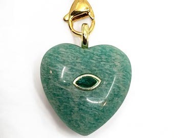 May include: A heart-shaped pendant made of green stone with a gold-colored bezel and chain. The pendant has a small, oval-shaped green stone in the center. The chain and clasp are gold-colored. The background is white.