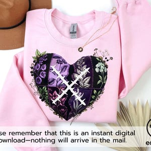 Puede incluir: Una sudadera rosa claro con un diseño en forma de corazón. El corazón está compuesto por varios parches florales y estampados en tonos morados, negros y blancos, con un diseño de punto de cruz blanco. También se ven un sombrero marrón y un collar dorado.