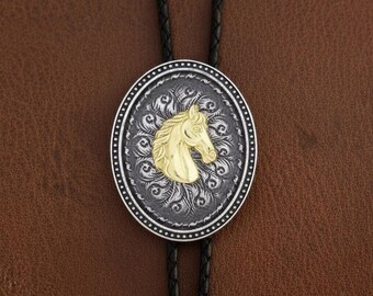 May include: Oval bolo tie with a gold horse head on a silver and black background. The horse head is centered on a decorative oval with a detailed border. The tie has a black leather cord.