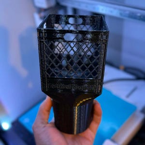May include: A black 3D-printed miniature milk crate with a diamond pattern and a handle. The crate is held up by a black base. The text "FestivalForge3D" is printed on the base.