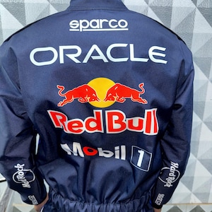 May include: Navy blue racing suit with the Sparco logo at the top and the Oracle and Red Bull logos in white and red. The sleeves have Hard Rock Cafe logos. The suit is a one-piece design.