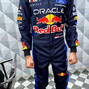 May include: Navy blue racing suit with multiple sponsor logos, including "Oracle" and "Red Bull." The suit features red, yellow, and white accents, with blue stripes down the sides of the legs. The suit has a zipper closure and a stand-up collar.