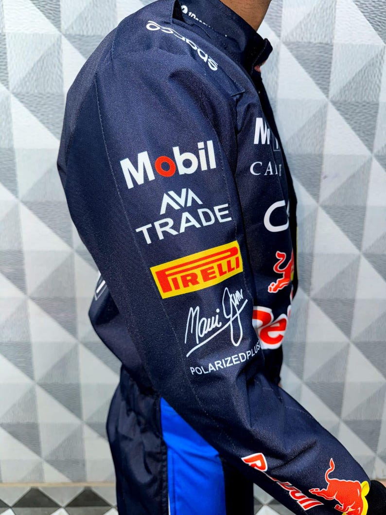 May include: Navy blue racing suit with sponsor logos including Mobil, Pirelli, and Ava Trade. The suit features a blue and red design with the words "Maui Jim" and "Polarizedplus" printed on the sleeve. The suit has a blue stripe down the side.