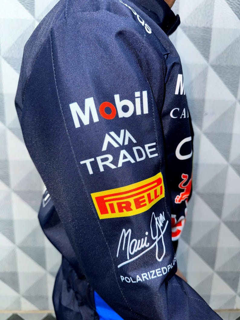 May include: Navy blue jacket with multiple sponsor logos, including "Mobil," "AVA TRADE," and "PIRELLI." The jacket features a signature and the text "POLARIZEDPLUS." The design incorporates red and white accents.