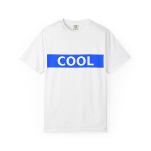Peut inclure: T-shirt blanc avec une bande horizontale bleue sur la poitrine. Le mot "COOL" est imprimé en lettres blanches dans la bande bleue. Le t-shirt a des manches courtes et un col rond.