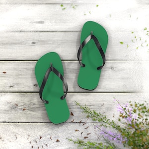 May include: A pair of flip-flops featuring solid green footbeds and black rubber straps. The footwear has a simple, flat design with a rounded toe area and a Y-shaped strap configuration that secures the foot to the sole for casual wear.