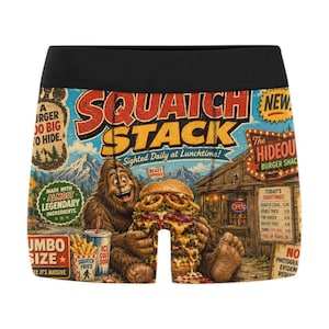 Peut inclure: Caleçon avec un imprimé graphique coloré représentant un Bigfoot mangeant un gros burger. Le motif inclut du texte comme SQUATCH STACK, The HIDEOUT BURGER SHACK et divers articles de menu sur un fond de montagnes et d'un bâtiment en bois.