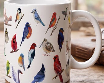 May include: A white ceramic mug featuring a detailed, colorful illustration of various bird species including a blue jay, a red cardinal, a swan, and other small songbirds scattered across the exterior surface with a curved handle on the right side.