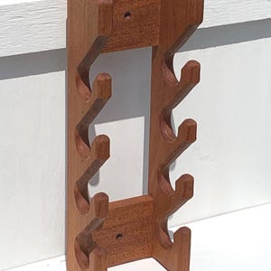 May include: A vertical wall-mounted wooden rack featuring a natural brown finish. The structure consists of two parallel side panels connected by top and bottom crossbars, each with three upward-curving hooks on both sides for storage.