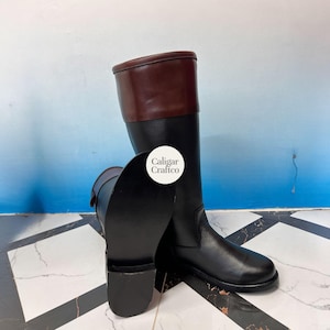 May include: A pair of black leather riding boots with a brown leather top. The boots are tall, with a classic design. The boots have a smooth finish and are suitable for equestrian activities.
