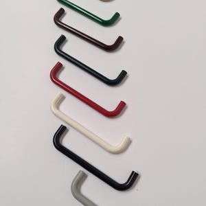 May include: A selection of curved metal handles in a range of colours: beige, green, brown, black, red, white, and grey. The handles are arranged diagonally, displaying their varied colour palette and design.