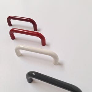 Może przedstawiać: Cztery uchwyty do szafek w kształcie litery U, ustawione w rzędzie. Uchwyty są w błyszczących kolorach: bordowym, czerwonym, białym i ciemnoszarym. Uchwyty te są prawdopodobnie przeznaczone do mebli lub szafek.