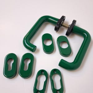 Op de afbeelding: Een set groene deurgrepen en sleutelgatdeksels. De handgrepen hebben een vierkante vorm met een gebogen greep. De sleutelgatdeksels zijn ovaal van vorm. De hardware heeft een glanzende, effen groene kleur.