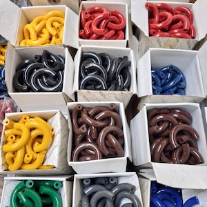 Pode incluir: Variedade de peças de plástico curvas e coloridas em caixas de cartão abertas. As cores incluem vermelho, amarelo, preto, azul, castanho, verde e cinzento. As peças parecem ser um componente de um produto ou sistema maior.