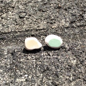 May include: Two small ceramic earrings, one with a white glaze and the other with a light green glaze.