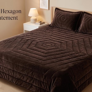 May include: A dark brown velvet quilt featuring a stitched hexagon pattern, accompanied by two matching velvet pillow shams. The text "Luxe Velvet Hexagon Quilt – A Statement in Comfort" is printed in the upper left corner of the image.