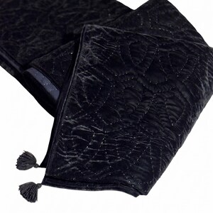 Puede incluir: Bufanda de terciopelo negro con un dise&ntilde;o acolchado y dos borlas. La bufanda est&aacute; doblada, mostrando la textura y el dise&ntilde;o. La tela tiene un brillo sutil, y las borlas est&aacute;n en los extremos.