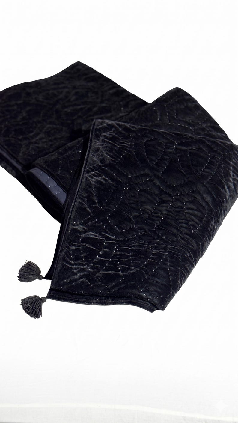 Puede incluir: Bufanda de terciopelo negro con un dise&ntilde;o acolchado y dos borlas. La bufanda est&aacute; doblada, mostrando la textura y el dise&ntilde;o. La tela tiene un brillo sutil, y las borlas est&aacute;n en los extremos.