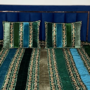 May include: A bed set featuring a quilt and two rectangular pillows made of velvet fabric in vertical stripes of dark green, teal, and olive. The stripes are separated by narrow bands of gold-toned metallic embroidery and sequins.