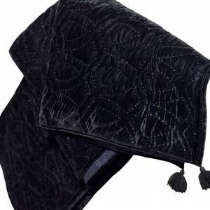 Puede incluir: Una manta negra de terciopelo con un patr&oacute;n acolchado y dos peque&ntilde;as borlas. La manta tiene un aspecto suave y texturizado y un color oscuro y lujoso. Las costuras son visibles, a&ntilde;adiendo detalles al dise&ntilde;o.