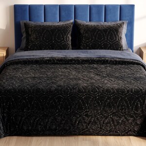 Puede incluir: Una cama con cabecero tapizado azul, con un edred&oacute;n gris oscuro y cojines decorativos a juego. El edred&oacute;n y las almohadas tienen un patr&oacute;n intrincado y brillante. Dos mesitas de noche de madera flanquean la cama.