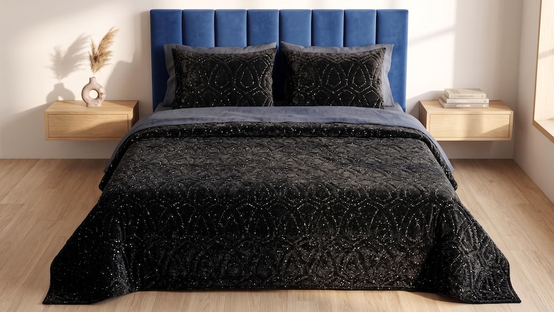 Puede incluir: Una cama con cabecero tapizado azul, con un edred&oacute;n gris oscuro y cojines decorativos a juego. El edred&oacute;n y las almohadas tienen un patr&oacute;n intrincado y brillante. Dos mesitas de noche de madera flanquean la cama.