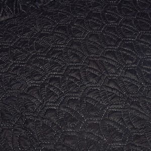 Puede incluir: Primer plano de una tela acolchada negra con un patr&oacute;n repetitivo en forma de hoja. Las costuras blancas crean contraste. La textura parece suave y afelpada.