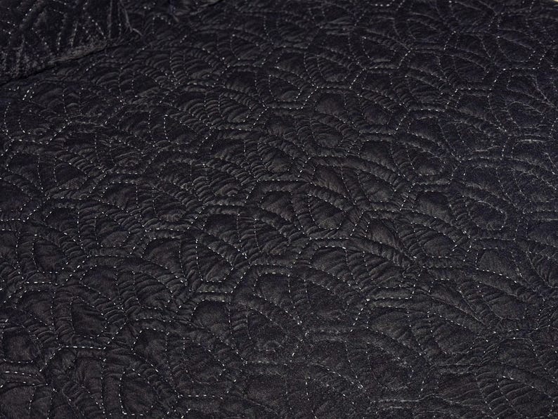 Puede incluir: Primer plano de una tela acolchada negra con un patr&oacute;n repetitivo en forma de hoja. Las costuras blancas crean contraste. La textura parece suave y afelpada.