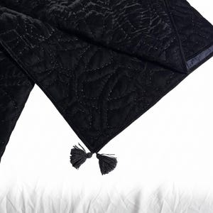 Puede incluir: Camino de mesa de terciopelo negro con un patr&oacute;n acolchado y borlas decorativas en los extremos. El camino de mesa est&aacute; hecho de una tela suave y texturizada.